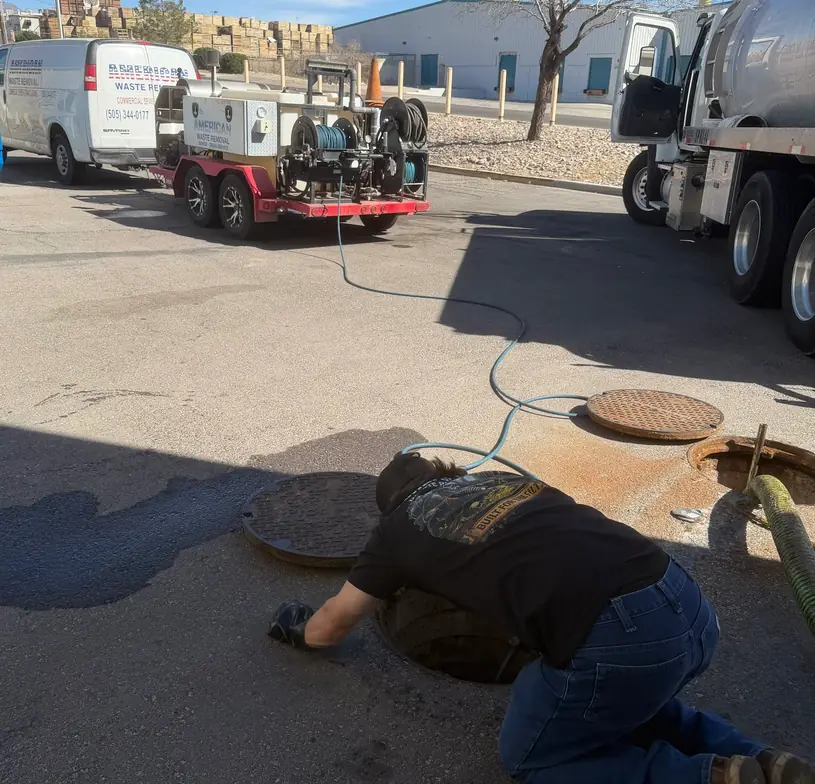 Red trailer-mounted hot-jet unit and jetter hose run to an open manhole