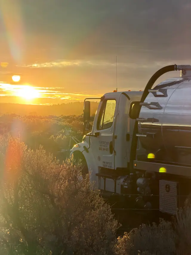 Vac truck cab and stainless tank backlit by the setting sun over high desert scrub