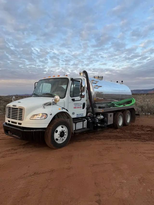 White vac truck with its hose coiled, parked on red dirt at dusk