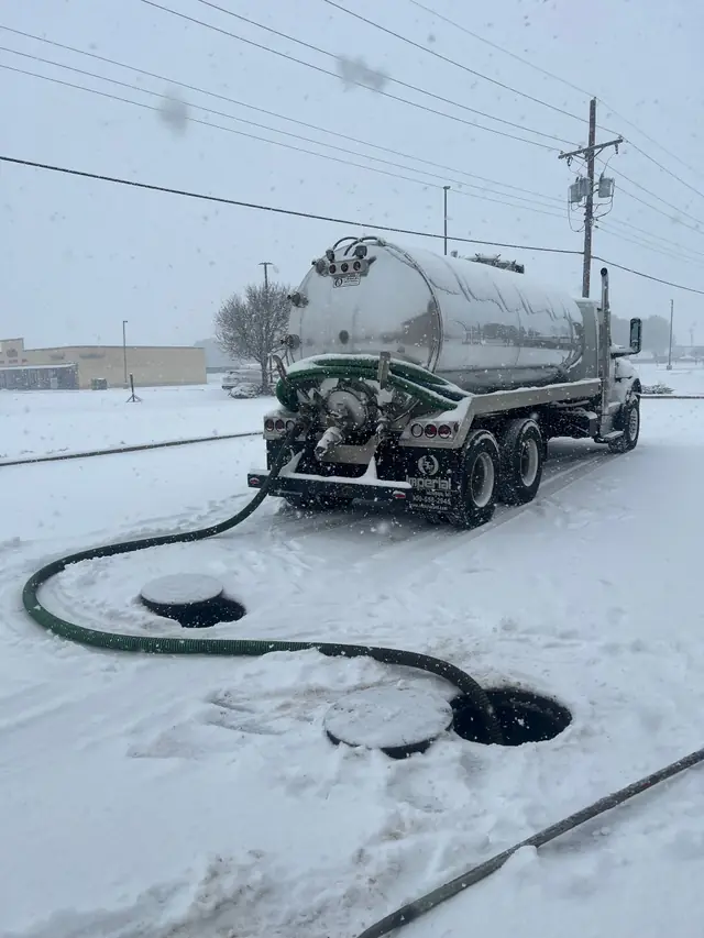 Vac truck pumping through an open lid with its hose laid across fresh snow